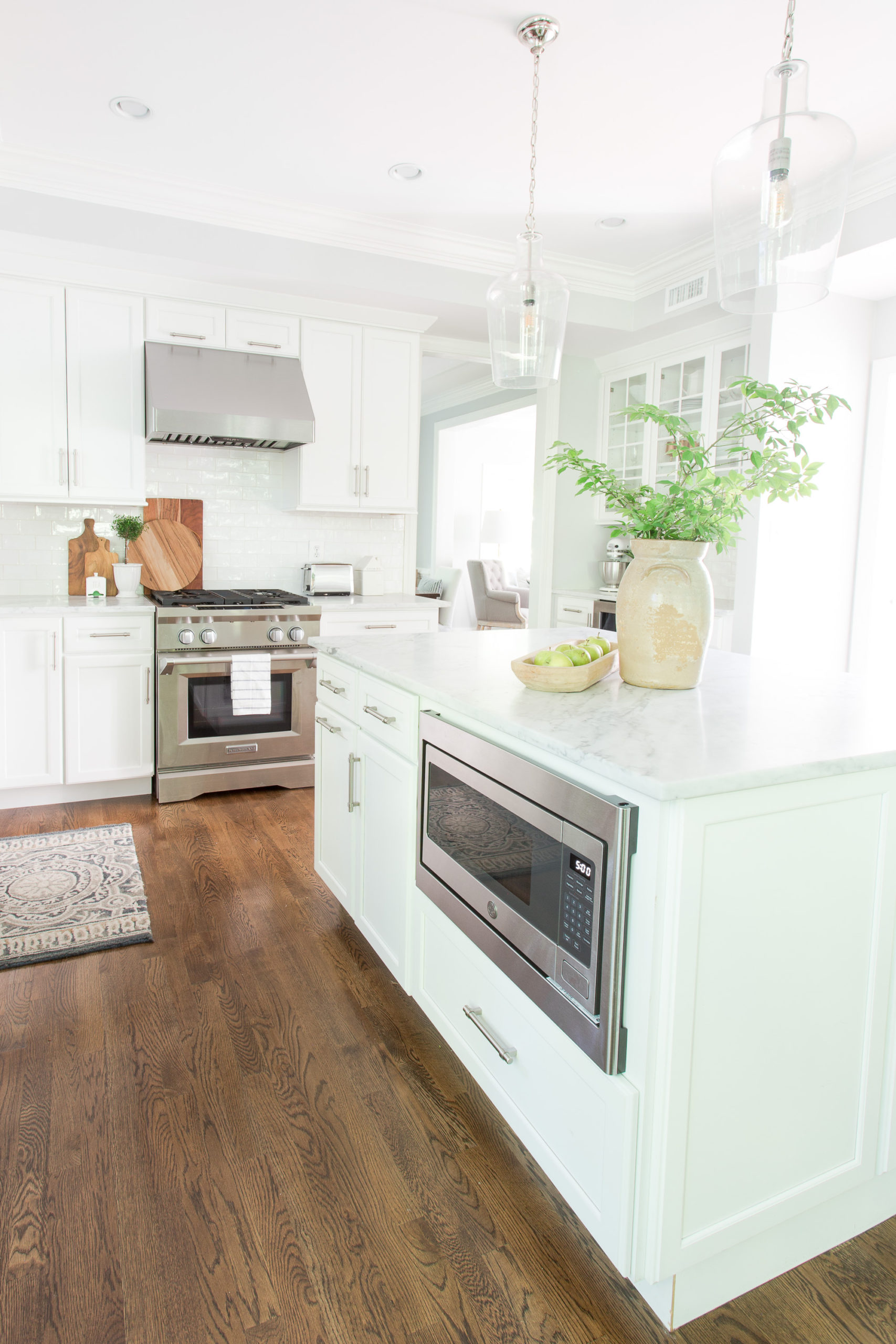 White kitchen looking at island with microwave, gas range and vase of greenery on island