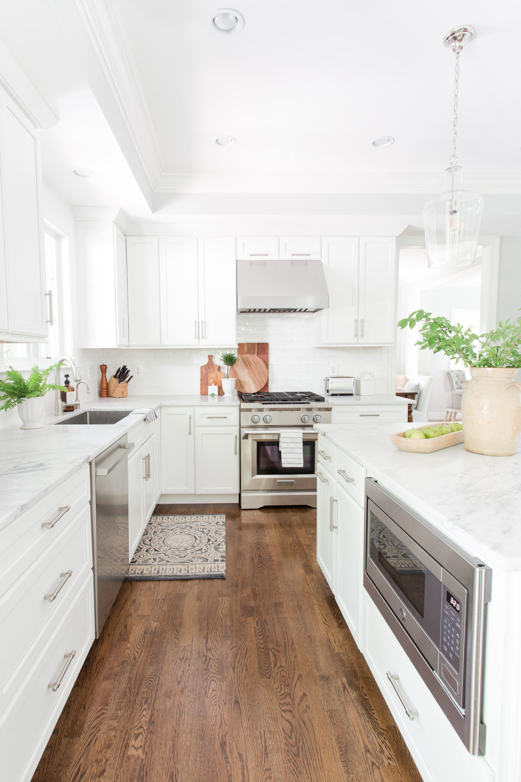 White kitchen with dark wood floors with microwave in island and stainless steel range with vase of greenery on island