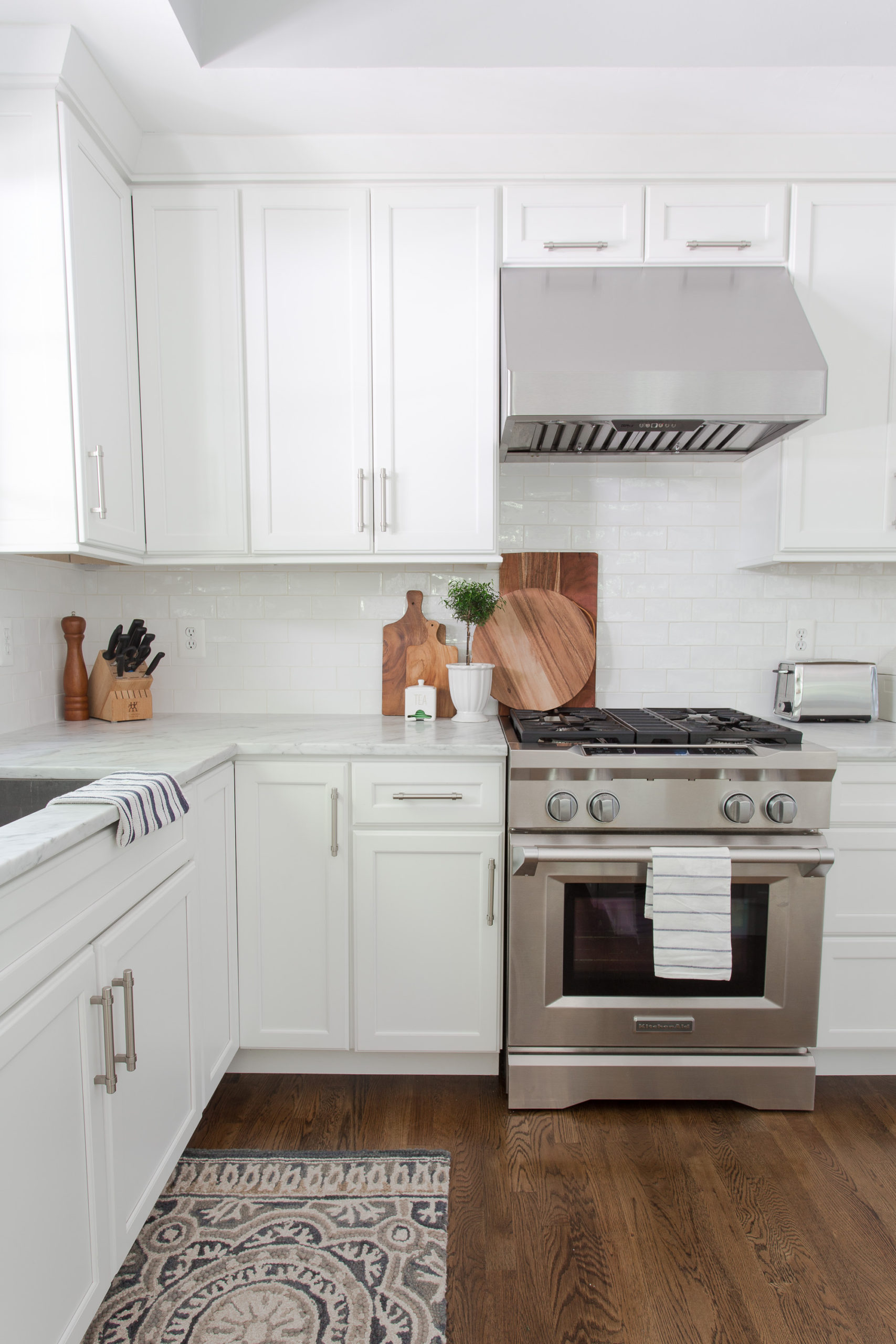 Stainless steel range in white kitchen with white tile backsplash and wooden tray leaning on the wall. 