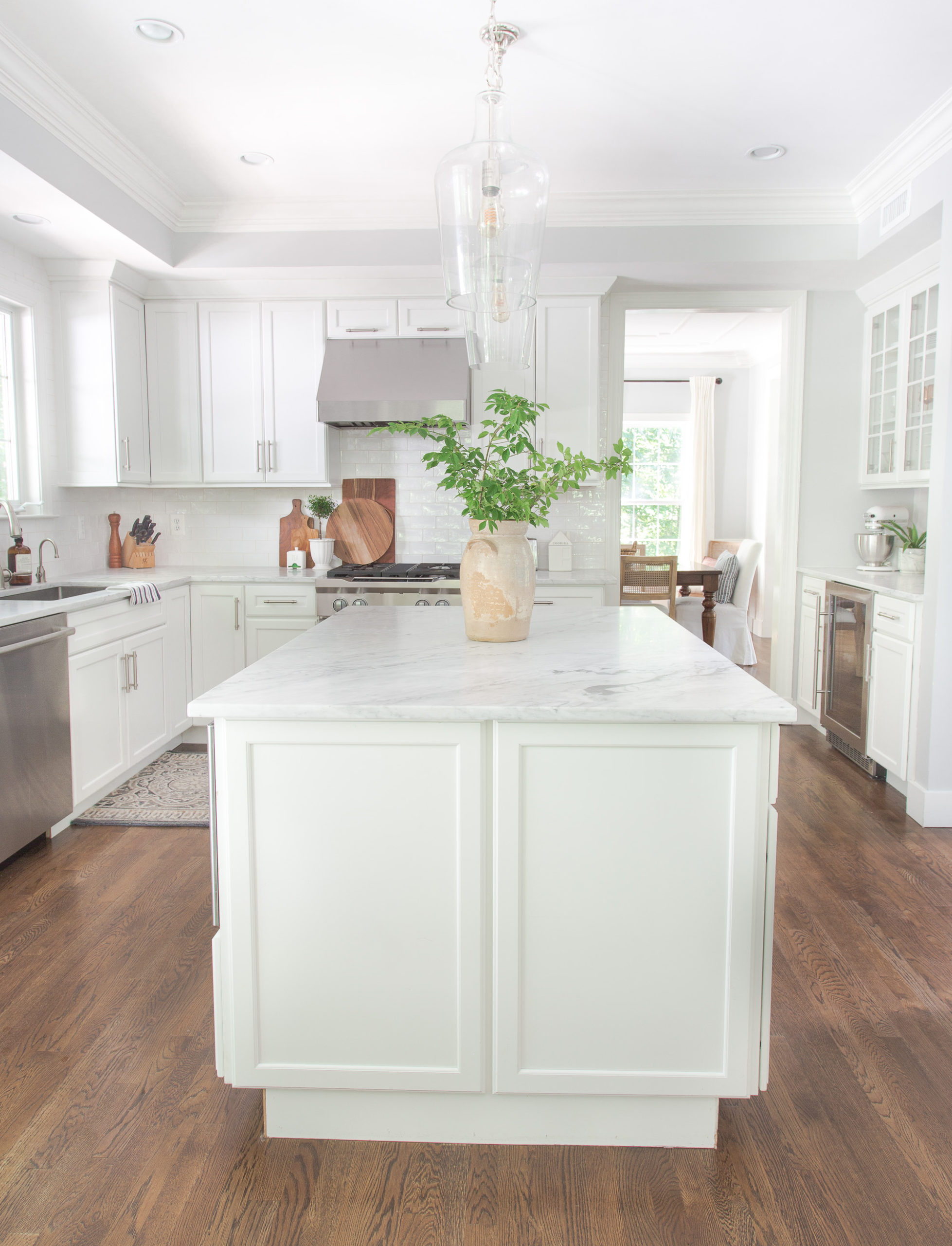 White kitchen with island with vase of greenery and dining in the background