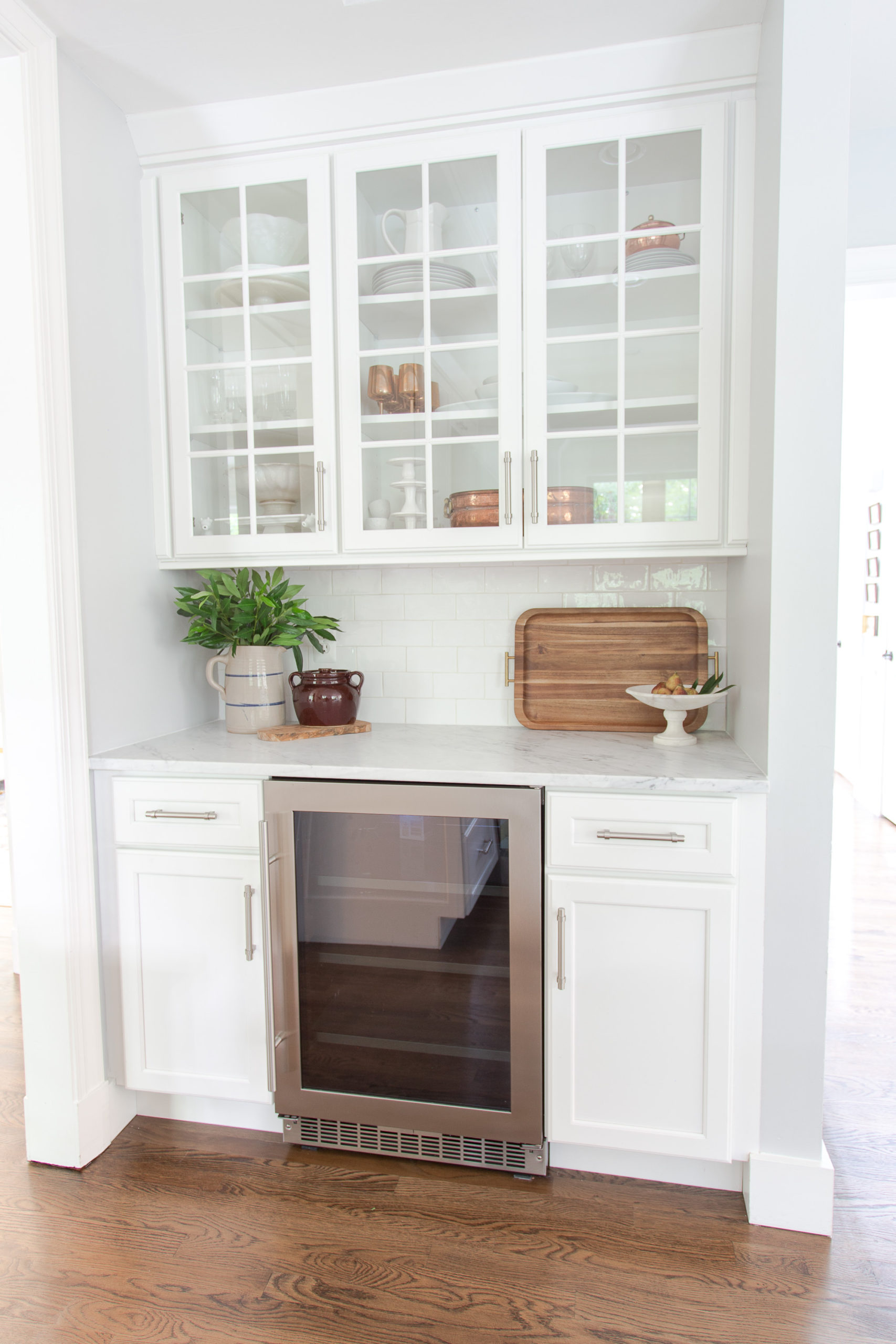 mini fridge in cabinets of a white kitchen with marble countertops