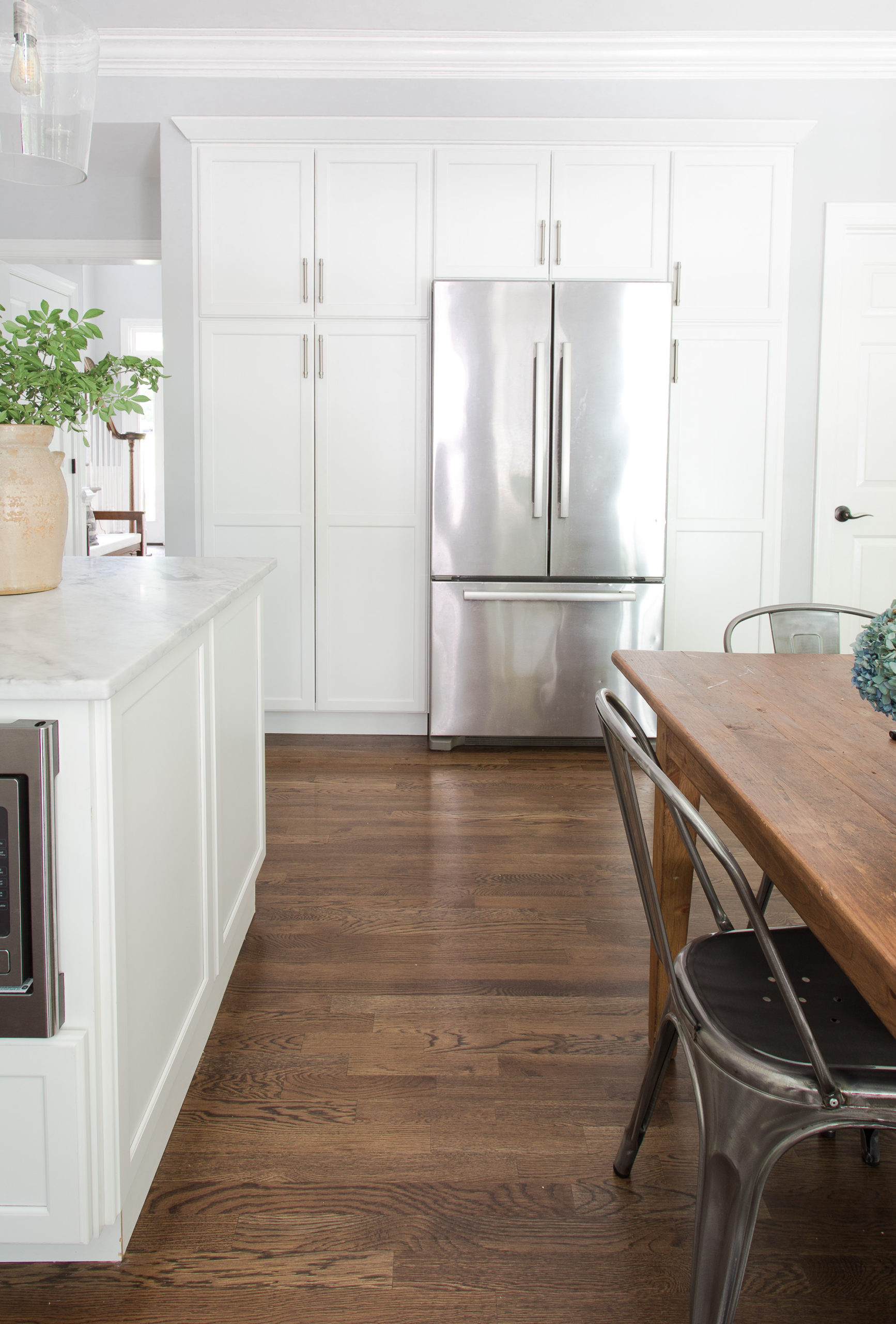 stainless steel fridge built into white kitchen cabinets with a wooden table and chairs near it. 