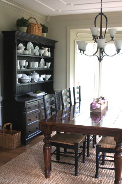 dining room with black china cabinet, jute rug, farmhouse table and black ladder back chairs